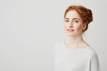 Wall Mural - Portrait of beautiful redhead girl with buns and freckles smiling looking at camera over white background.