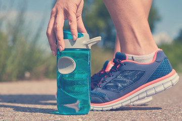 young girl takes sports bottle of water to drink, feet in sneakers