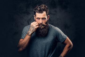 A man touches his moustache over grey background.