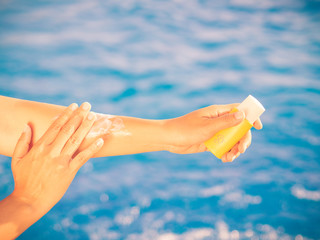 Wall Mural - Woman hand apply sunscreen / sunblock by the swimming pool. Vacation and relaxation, summer travel concept.