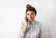 © shurkin_son - People, technology and communication concept. Funny cute young Caucasian female secretary with hair knot wearing formal shirt talking on mobile phone, listening attentively to her interlocutor