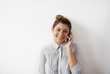 © shurkin_son - Happy young woman employee having nice phone conversation in office. Cheerful student girl in blouse talking on mobile phone, smiling, standing at studio wall with copy space for your text or content