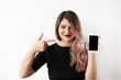 © shurkin_son - Cheerful cute young woman with colored pink hair standing isolated at studio wall, holding generic smart phone and pointing finger at its blank screen, showing copyspace for your promotional content