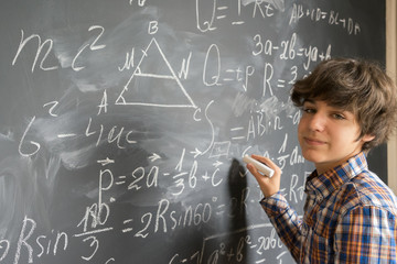 Handsome teenage Boy with chalk writting complicated math formulas on black board