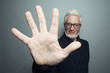 © Augustino - Funny old hipster concept. Portrait of 60-year-old man standing over gray background and giving five. Close up. Studio shot