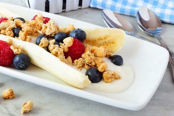 Wall Mural - healthy banana split with yogurt, fresh berries and granola, close up scene over marble