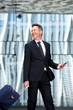 © mimagephotos - Happy business man walking with suitcase and mobile phone