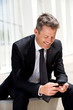 © mimagephotos - Businessman sitting and smiling holding mobile phone