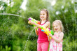 © MNStudio - Adorable little girls playing with water guns on hot summer day. Cute children having fun with water outdoors.