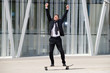 © mimagephotos - Full length fun businessman standing on skateboard with arms raised