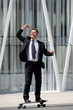 © mimagephotos - Full length fun businessman standing on skateboard with arm outstretched