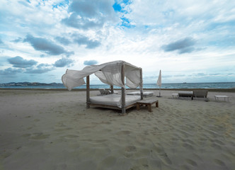 Big sun bed alcove on the windy sand shore, fluttering in the wind, waving, raising white curtains, Ibiza, Spain, landscape, mood, no people, cloudy sky..
