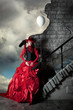 Woman in a red historic dress is standing on a background of a stormy sky near a stone wall with a white balloon.