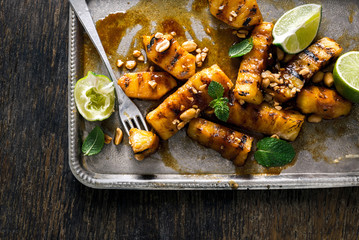 Tray of caramelized grilled pineapple with nuts and lime closeup