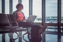 Young Beautiful Woman Traveler Sits At The Airport With A Laptop While Waiting For Her Flight