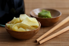 Pickled Ginger Slices In Wooden Bowl On Bamboo Mat Next To Chopsticks, Wasabi Paste And Bottle Of Soya Sauce.