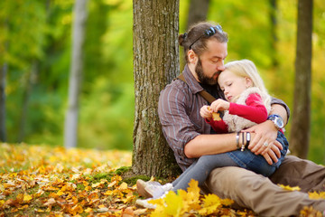 Wall Mural - Cute little girl and her father having fun on beautiful autumn day. Happy child playing in autumn park. Kid gathering yellow fall foliage.