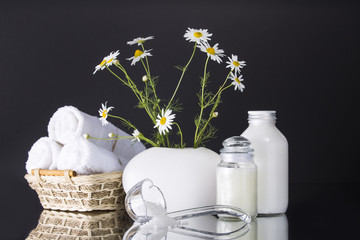 Spa. Chamomile in a vase, three white towels rolled into a roll lie in a basket. Two cans of cream. Salt in a transparent scoop.