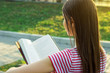 © sosiukin - Back view of lovely young girl with long beautiful hair reading a book outside