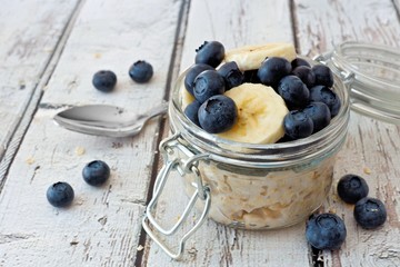 Wall Mural - overnight oats with fresh blueberries and bananas in a jar on a rustic white wood background