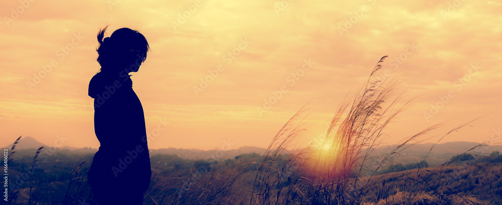 A woman standing alone in sunset scene. - obrazy, fototapety, plakaty 