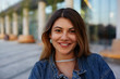 © shurkin_son - Headshot of attractive latin woman with pretty face looking and smiling cheerfully at camera, posing in urban surroundings on summer day, wearing trendy accessories and denim jacket. City lifestyle