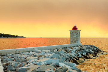 Wall Mural - Lighthouse in the harbor of a small town Postira shot at sunset - Croatia, island Brac