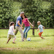 © jackfrog - Cheerful family playing football in a garden