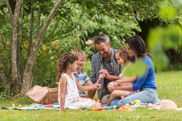 Wall Mural - Cheerful family sitting on the grass during un picnic in a park