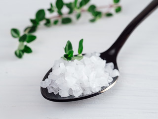 Wall Mural - coarse sea salt in black spoon on white background with thyme. Copy space.