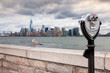 Binoculars on Ellis Island pointed towards Manhattan's skyline in a cloudy day