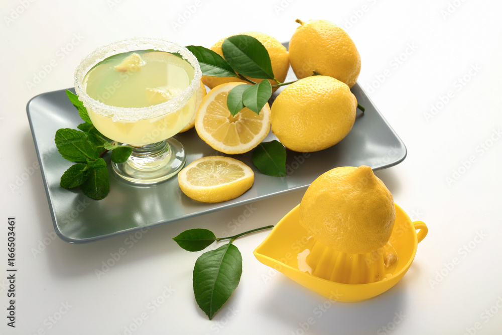 Platter with glass of juice, lemons and squeezer on white background