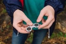 Young Man Holds A Spinner. Natural. Popular Spinner Gadget. Man Holds A Metal Gray Spinner. Autumn Background