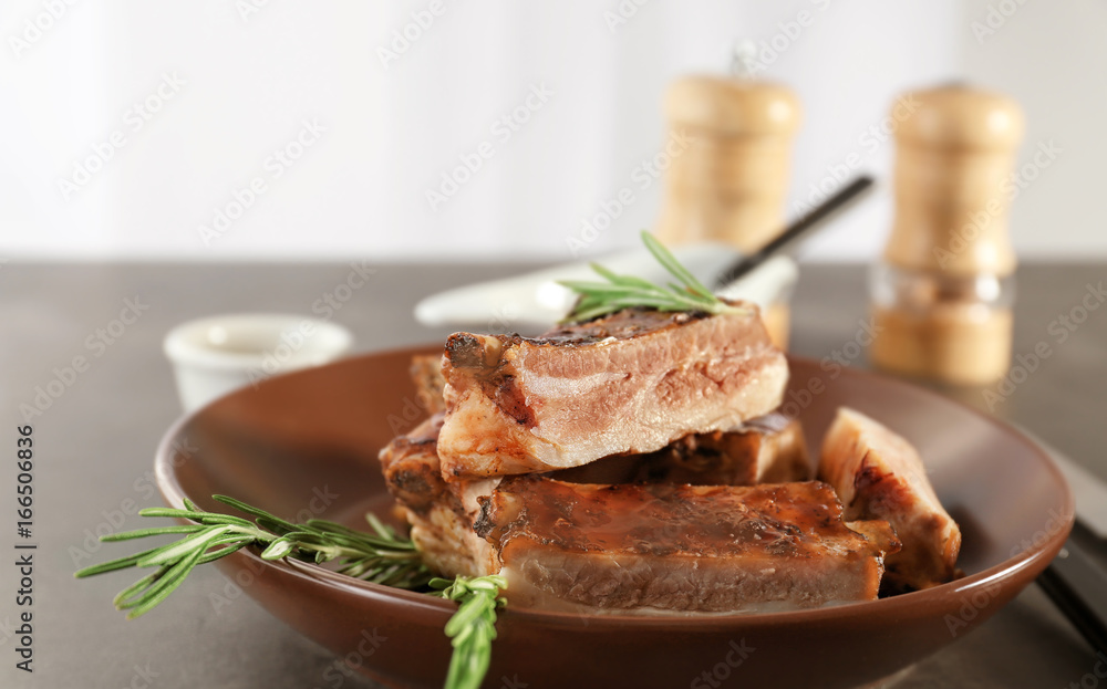 Plate with delicious pork ribs and rosemary on table