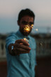 © BONNINSTUDIO/Stocksy - Young man covering his face with a sparkler at evening.