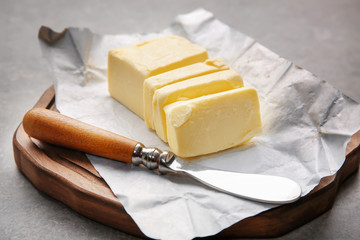 Poster - Cutting board with piece of unwrapped sliced butter and knife on grey background