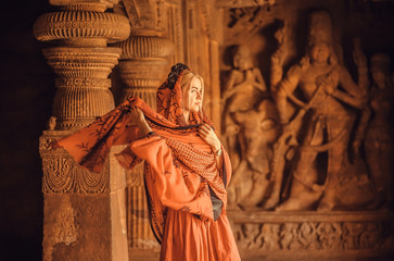 Woman in red scarf walking inside the 6th century Hindu temple with ancient caves and artworks, Karnataka of India