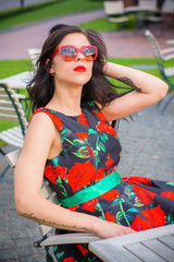 Gorgeous vintage brunette woman with curly hair on a style 50s in black dress with red roses. Pretty girl walk on a streets and have a good mood feeling wonderful