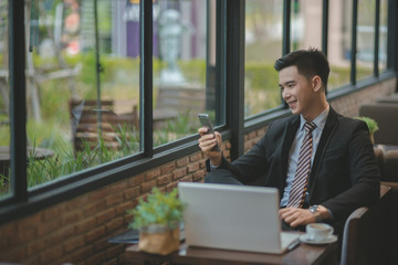 Happy  businessman using cellphone while sitting on sofa at his modern home.Concept of young people working on mobile devices.Blurred background