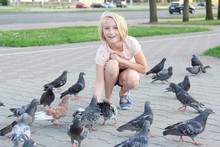 Cheerful Girl Feeds Pigeons On The Street In The City