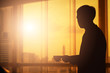 © Love You Stock - silhouette businessman holding coffee cup looking out over the city through office transparent glass window at sunset time. Coffee break concept.