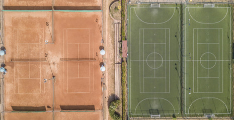 Vista aerea perpendicolare di due campi di calcio a 5 e un campo da tennis in terra rossa. A bordo campo panchine e ombrelli. I campi sono vuoti perchè è estate e fa caldo.