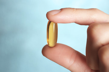 Wall Mural - Fish oil pill in female hand on light background