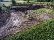 Top View Heavy Machine Excavator Bagger Working In Mud On Construction Site With Green Landscape Surrounding