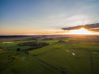 Wall Mural - 
aerial view of a beautiful sunset with sunbeams above green agricultural fields in the summer