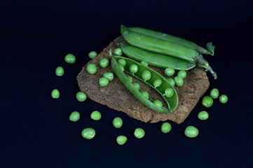 Pods of fresh green pea and individual peas on a black backgroun