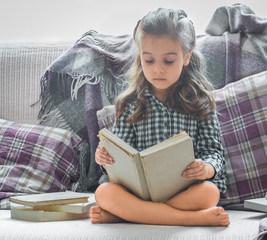 Wall Mural - little girl reading book on sofa