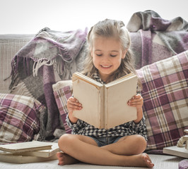 Wall Mural - little girl reading book on sofa