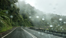 The Rain Drops On The Windshield Of The Car. Selective Focus On The Curved Road On Background. Dangerous Vehicle Driving In The Heavy Rainy And Slippery Road Concept. Borneo Island, Sabah, Malaysia