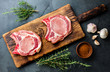 Raw pork cutlet chop for fry on pan with herbs, garlic on wooden boards, slate gray background